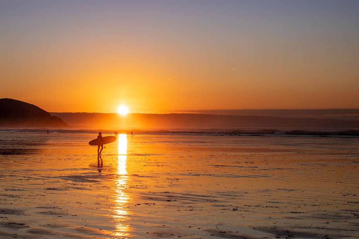 Person walking to ocean with surfboard in North Devon